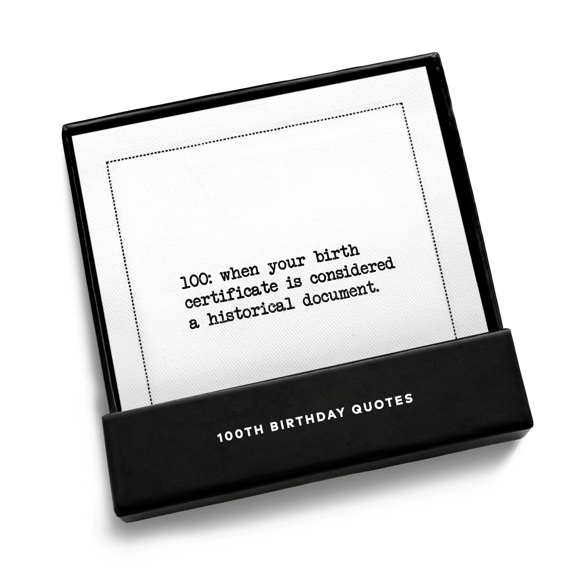 Open black gift box from Five Star Napkins' 100th birthday quote collection, revealing an organic cotton cocktail napkin printed with the quote "100: when your birth certificate is considered a historical document"