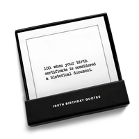 Open black gift box from Five Star Napkins' 100th birthday quote collection, revealing an organic cotton cocktail napkin printed with the quote "100: when your birth certificate is considered a historical document"