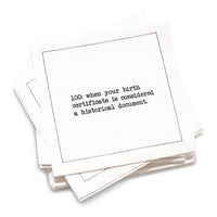 Organic cotton cocktail napkin with black dotted border printed with the quote "100: when your birth certificate is considered a historical document," from Five Star Napkins' 100th birthday quote collection