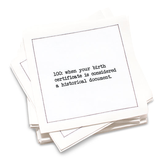 Organic cotton cocktail napkin with black dotted border printed with the quote "100: when your birth certificate is considered a historical document," from Five Star Napkins' 100th birthday quote collection