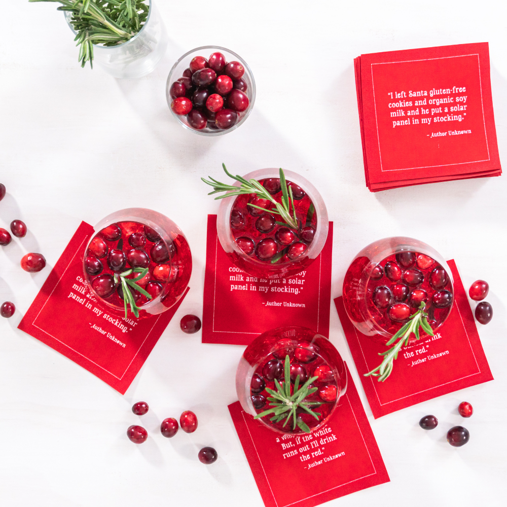 Persimmon organic cotton cocktail napkins with printed holiday quotes, shown under drinks with cranberries and rosemary, festive entertaining setting.