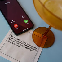 Organic cotton cocktail napkin with printed quote, amber stem glass, and smartphone on table