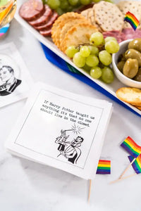 Stack of organic cotton quote napkins reading 'If Harry Potter taught us anything it’s that no one should live in the closet' next to a charcuterie board and rainbow flags at a cocktail party setting.