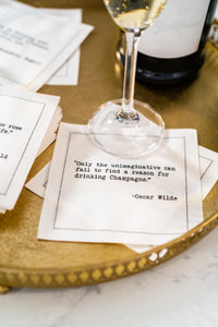 Organic cotton cocktail napkin with Oscar Wilde quote beside a champagne glass on a gold tray
