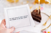 Organic cotton cocktail napkin with printed quote, 'You know you're 50 when a kid you once babysat is now your lawyer,' shown at a birthday table setting.