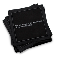 Stack of black 30th birthday quote cocktail napkins with white typewriter-style text reading, “I’m not 30. It’s my 1st anniversary of my 29th birthday.”