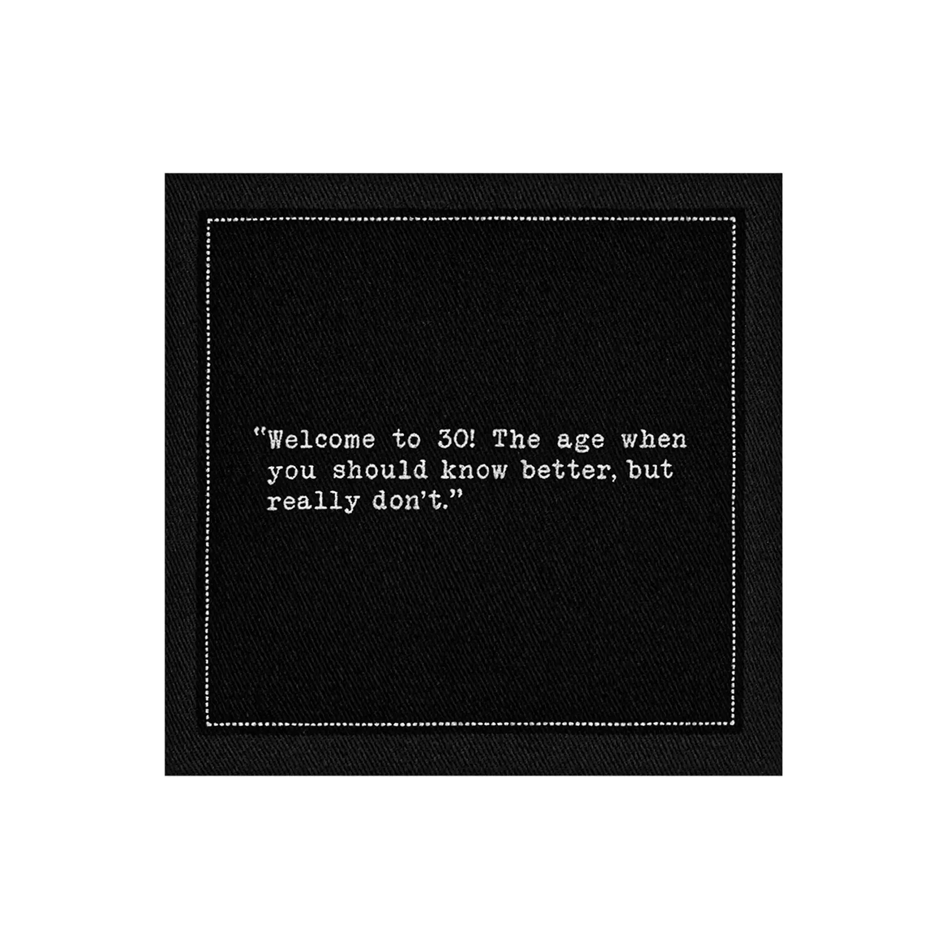 Black 30th birthday quote cocktail napkin with white typewriter-style text reading, “Welcome to 30! The age when you should know better, but really don’t.”