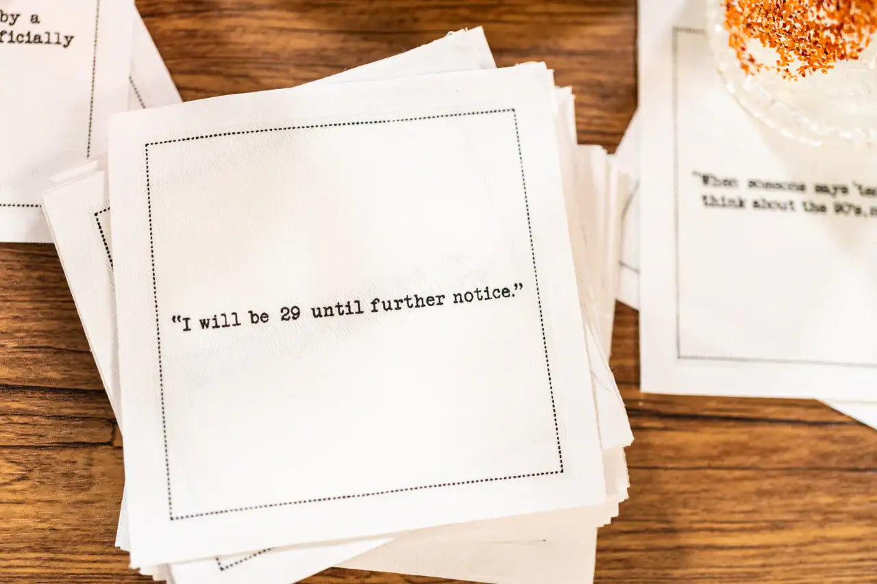 Stack of white 30th birthday quote cocktail napkins with black typewriter-style text reading, “I will be 29 until further notice.”