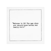 White 30th birthday quote cocktail napkin with black typewriter-style text reading, “Welcome to 30! The age when you should know better, but really don’t.”