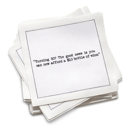 Stack of white 30th birthday quote cocktail napkins with black typewriter-style text reading, “I’m not 30. It’s my 1st anniversary of my 29th birthday.”