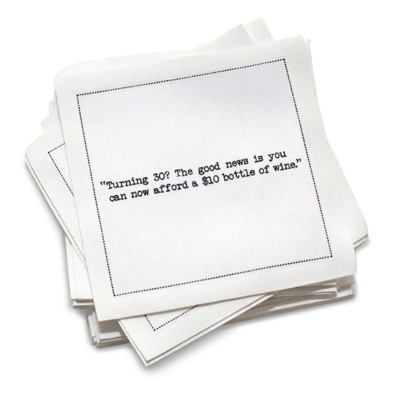 Stack of white 30th birthday quote cocktail napkins with black typewriter-style text reading, “I’m not 30. It’s my 1st anniversary of my 29th birthday.”