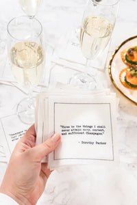 Hand holding organic cotton napkin with quote, champagne glasses, hors d'oeuvres on marble table
