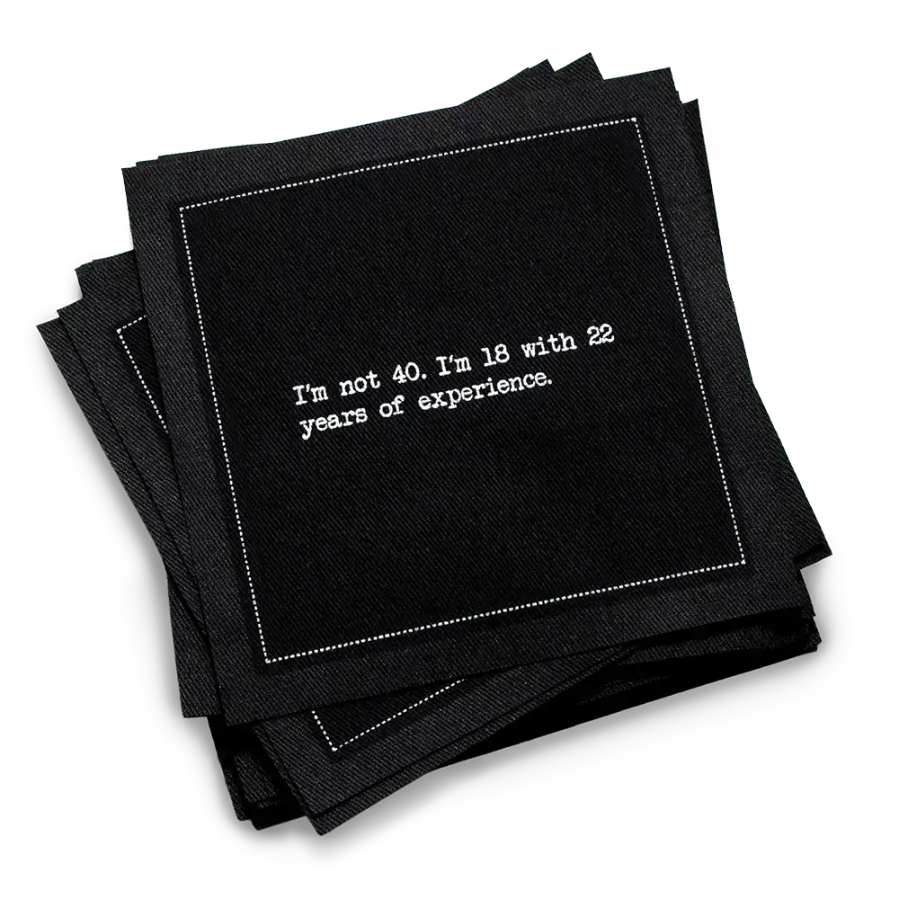 Organic cotton cocktail napkin, black, with white dotted border printed with the quote "I'm not 40. I'm 18 with 22 years of experience," from Five Star Napkins' 40th birthday quote collection