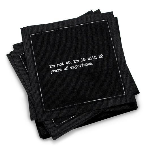 Organic cotton cocktail napkin, black, with white dotted border printed with the quote "I'm not 40. I'm 18 with 22 years of experience," from Five Star Napkins' 40th birthday quote collection