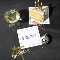 Organic cotton cocktail napkin printed with the quote "Inside every 40 year old is a teenager wondering, 'what on Earth happened?'" styled on a dark table with birthday cake, champagne, a disco ball, and a "Happy Birthday" cake topper, from Five Star Napkins' 40th Birthday Quotes collection