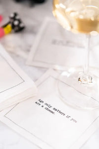 Organic cotton cocktail napkin printed with the quote "Age only matters if you are a cheese," styled under a wine glass on a marble table with birthday party decor, from Five Star Napkins' 40th Birthday Quotes collection