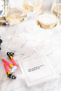 Organic cotton cocktail napkin printed with the quote "Looks 18...Feels 14...Acts 8. That makes me 40!" styled on a marble table with wine glasses and party blowers, from Five Star Napkins' 40th Birthday Quotes collection