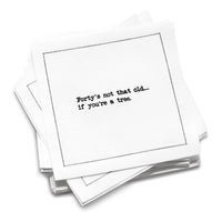 A stack of white 40th Birthday Quotes cocktail napkins with black dotted borders. The top napkin reads, “Forty’s not that old… if you’re a tree.”