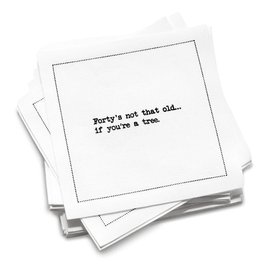 A stack of white 40th Birthday Quotes cocktail napkins with black dotted borders. The top napkin reads, “Forty’s not that old… if you’re a tree.”