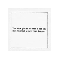 Organic cotton cocktail napkin with black dotted border printed with the quote "You know you're 50 when a kid you once babysat is now your lawyer," from Five Star Napkins' 50th Birthday Quotes collection