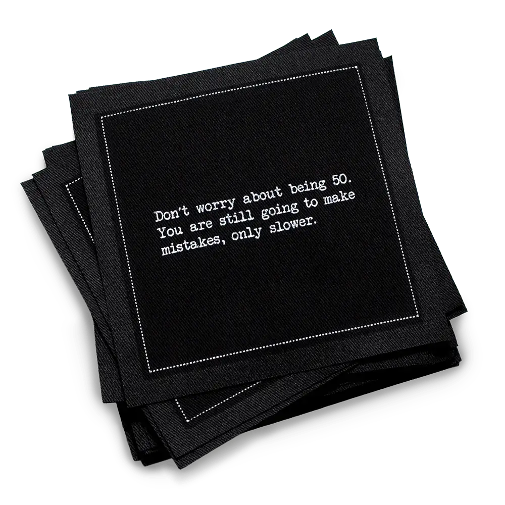 Organic cotton cocktail napkin, black, with white dotted border printed with the quote "Don't worry about being 50. You are still going to make mistakes, only slower," from Five Star Napkins' 50th birthday quote collection