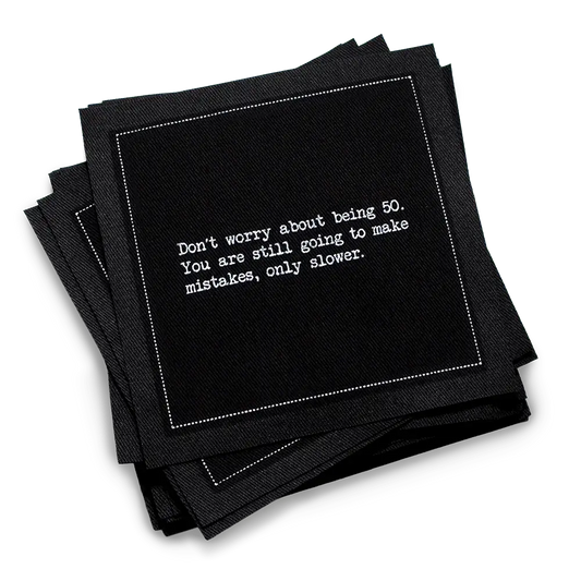 Organic cotton cocktail napkin, black, with white dotted border printed with the quote "Don't worry about being 50. You are still going to make mistakes, only slower," from Five Star Napkins' 50th birthday quote collection
