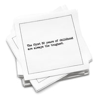 Stack of white organic cotton cocktail napkins with black dotted border printed with the quote “The first 50 years of childhood are always the toughest,” from Five Star Napkins' 50th birthday quote collection