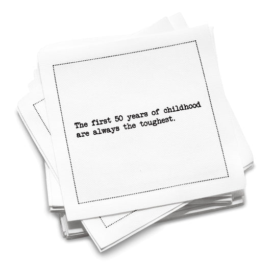 Stack of white organic cotton cocktail napkins with black dotted border printed with the quote “The first 50 years of childhood are always the toughest,” from Five Star Napkins' 50th birthday quote collection