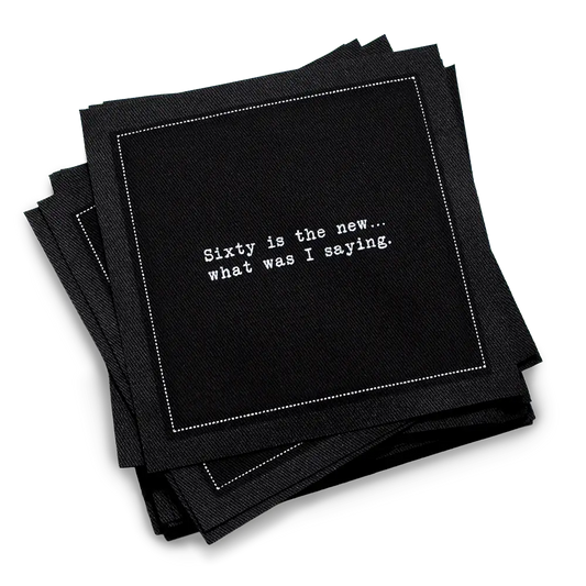 Organic cotton cocktail napkin, black, with white dotted border printed with the quote "Sixty is the new... what was I saying," from Five Star Napkins' 60th birthday quote collection