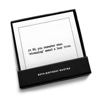 Black gift box from Five Star Napkins' 80th birthday quote collection, open to display an organic cotton cocktail napkin printed with the quote "At 80, you remember when 'streaming' meant a lazy river,'"