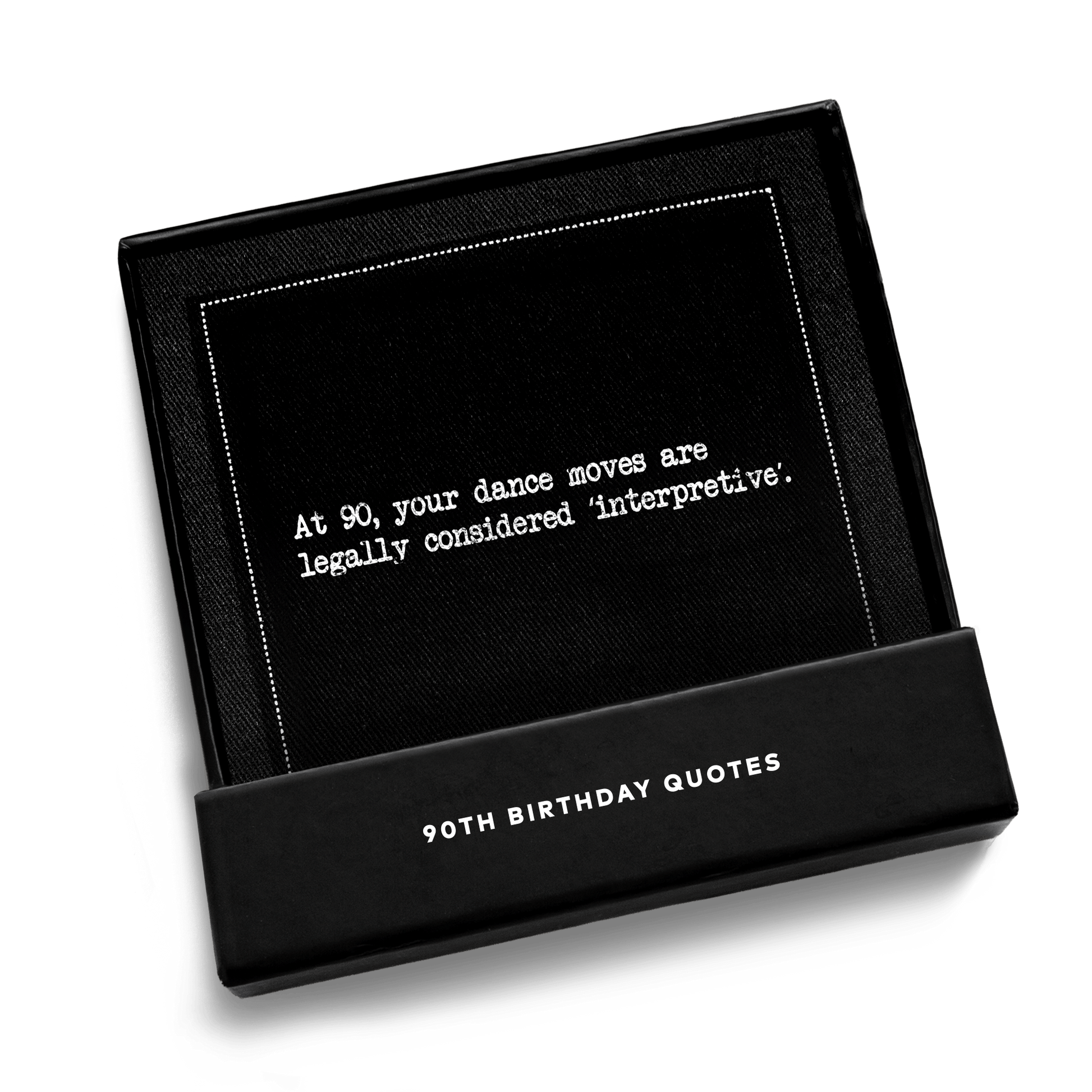 Open black gift box from Five Star Napkins' 90th birthday quote collection, revealing an organic cotton cocktail napkin, black, printed with the quote "At 90, your dance moves are legally considered 'interpretive,'"