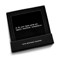 Open black gift box from Five Star Napkins' 90th birthday quote collection, revealing an organic cotton cocktail napkin, black, printed with the quote "At 90, your dance moves are legally considered 'interpretive,'"