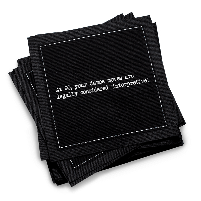 Organic cotton cocktail napkin, black, with white dotted border printed with the quote "At 90, your dance moves are legally considered 'interpretive,'" from Five Star Napkins' 90th birthday quote collection
