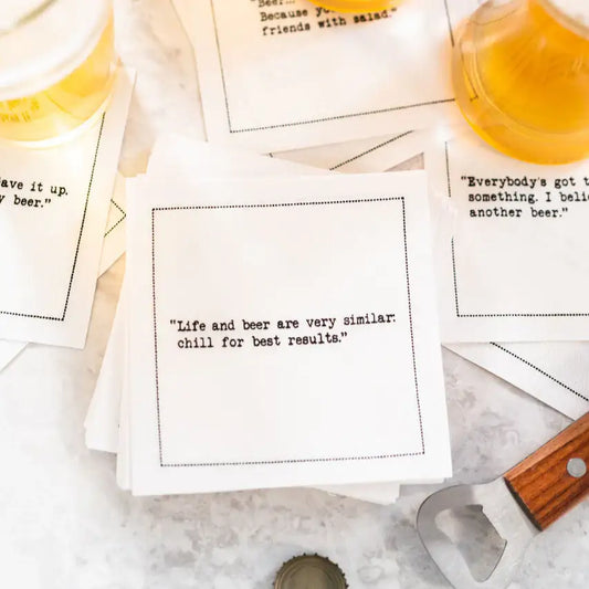 White Beer Quotes cocktail napkins scattered beside glasses of beer and a bottle opener. The center napkin reads, “Life and beer are very similar: chill for best results.”
