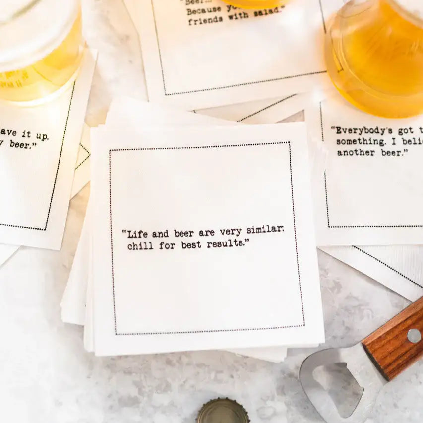 White Beer Quotes cocktail napkins scattered beside glasses of beer and a bottle opener. The center napkin reads, “Life and beer are very similar: chill for best results.”