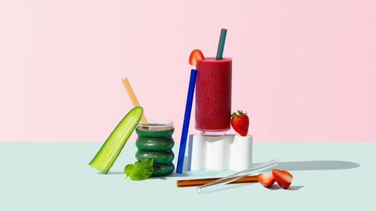 Reusable glass smoothie straws styled with smoothies, cucumber, mint, and strawberries, by Five Star Napkins.