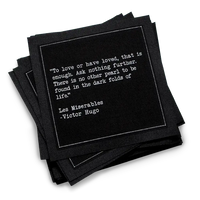 A stack of black Love Quotes cocktail napkins with white dotted borders. The top napkin features a Victor Hugo quote from Les Misérables: “To love or have loved, that is enough. Ask nothing further.”