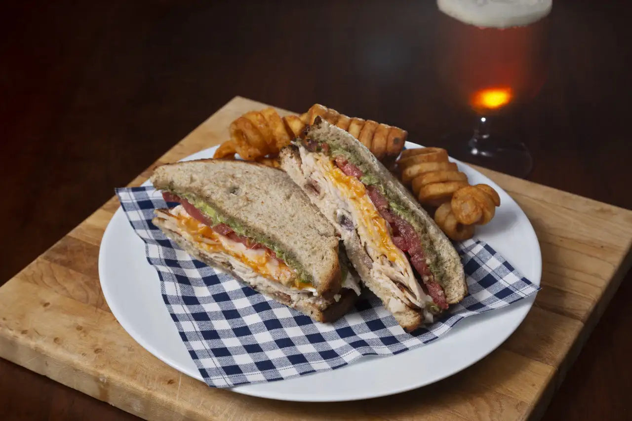 Blue and white checkered organic cotton napkin under sandwich and curly fries on plate