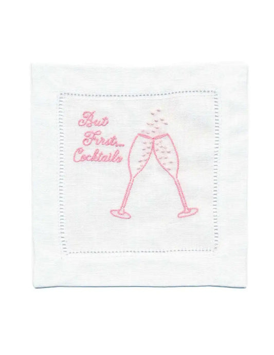 Organic cotton cocktail napkin with pink embroidery, featuring 'But First... Cocktails' quote and two glasses.