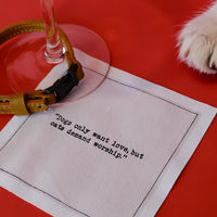 Organic cotton cocktail napkin with quote 'Dogs only want love, but cats demand worship,' cat paw, wine glass on red surface.