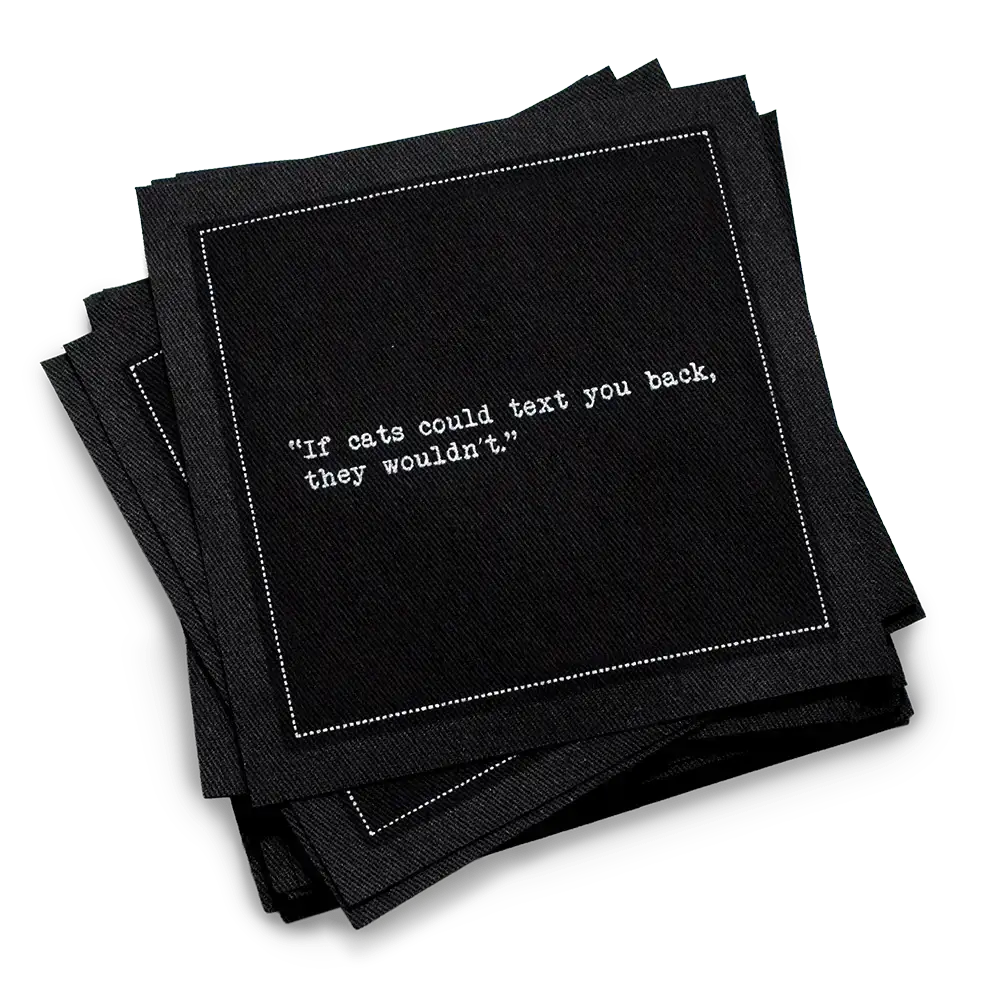 Stack of black organic cotton cocktail napkins with white dotted border printed with the quote “If cats could text you back, they wouldn't,” from Five Star Napkins' Cat quote collection