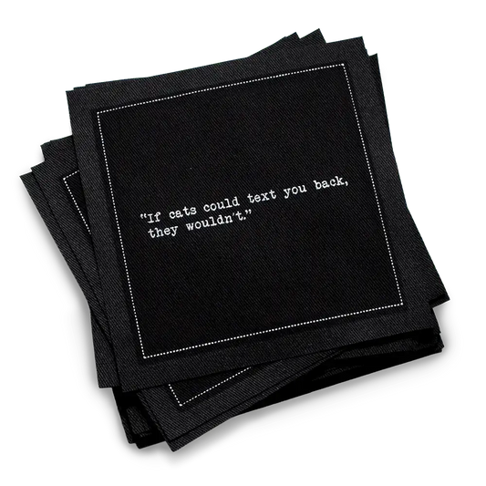 Stack of black organic cotton cocktail napkins with white dotted border printed with the quote “If cats could text you back, they wouldn't,” from Five Star Napkins' Cat quote collection