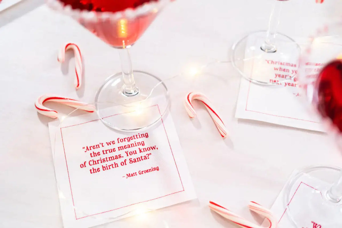 Organic cotton quote napkin with red text, Matt Groening Christmas quote, cocktail party setting with candy canes and drinks