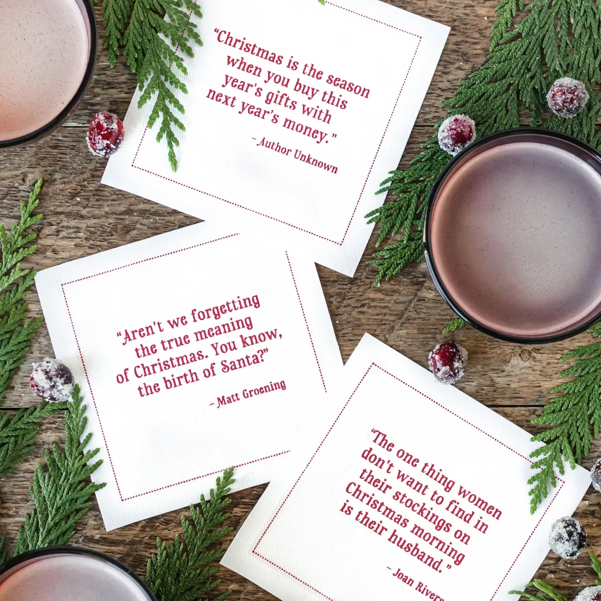 Organic cotton cocktail napkins in white with red printed Christmas quotes, styled for a holiday cocktail party with greenery and drinks.