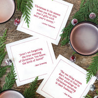 Organic cotton cocktail napkins in white with red printed Christmas quotes, styled for a holiday cocktail party with greenery and drinks.