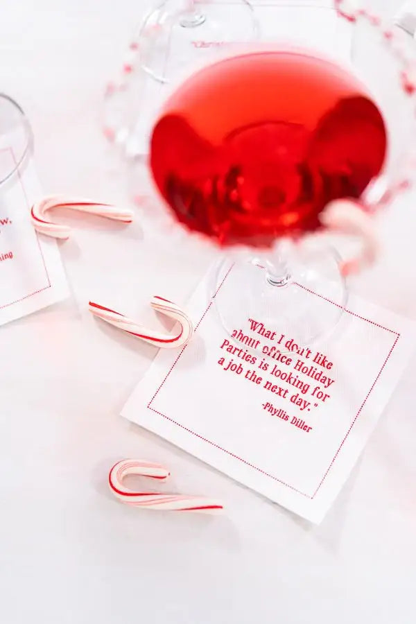 Organic cotton cocktail napkin in white with red quote, crystal glass of red drink, mini candy canes on table, holiday party setting