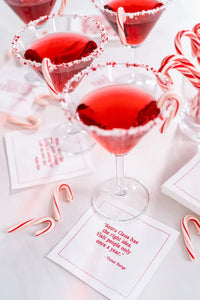 Holiday cocktail party setting with red drinks, candy canes, and organic cotton quote napkins reading 'Santa Claus has the right idea. Visit people only once a year.'