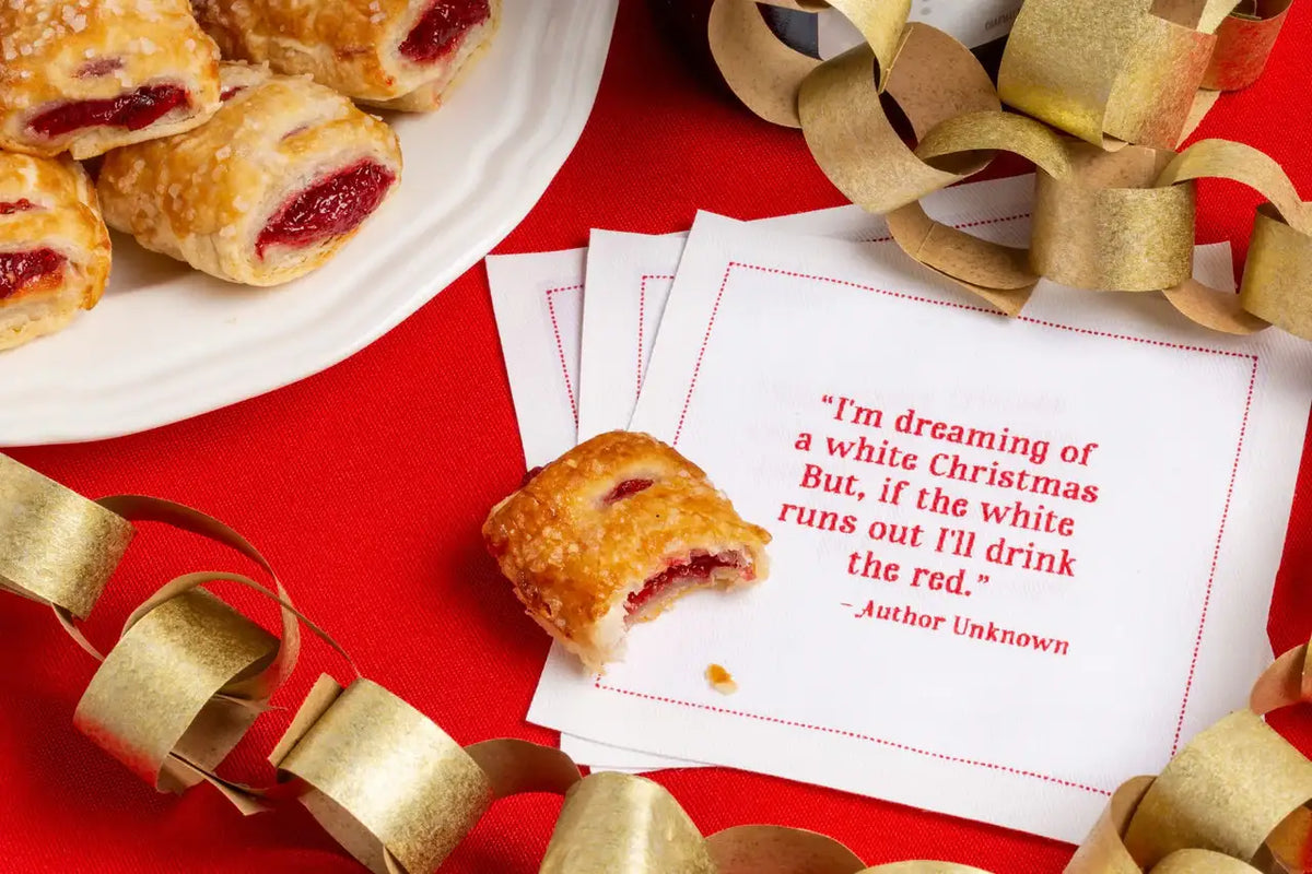 White organic cotton napkin with red quote text, pastries, gold paper chain, holiday party table