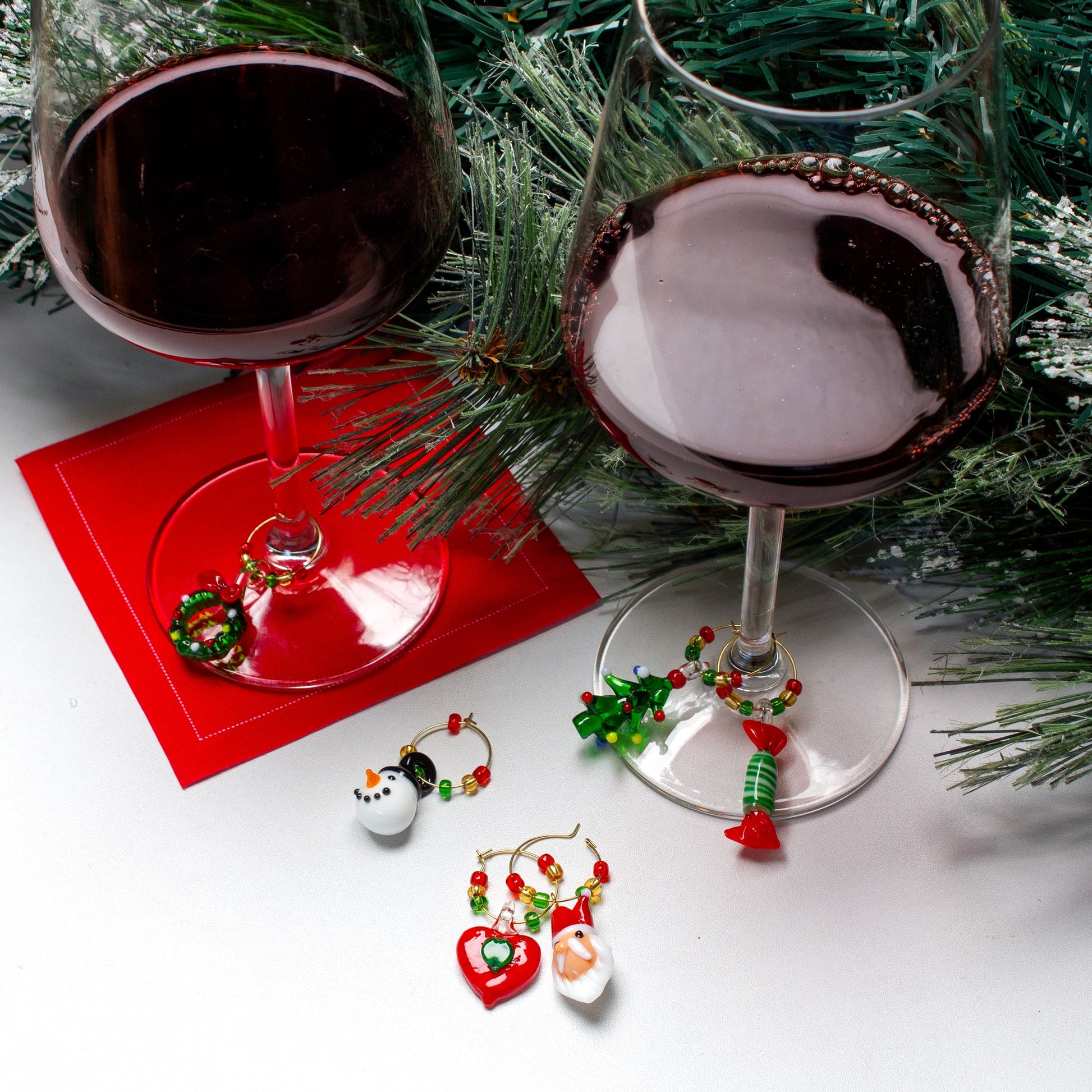 Two wine glasses with Christmas-themed wine charms on a white surface with greenery.