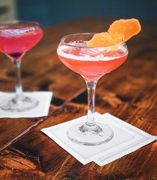 Cosmopolitan cocktails served on ecru organic cotton cocktail napkins at a rustic wood bar table.